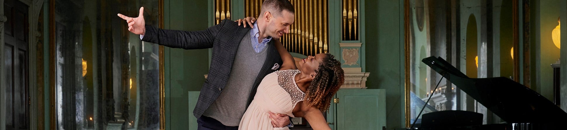 A couple dancing under a chandelier and a piano and organ in the background