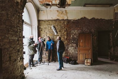 Film crew of three film one subject in a room that's undergoing renovation work.