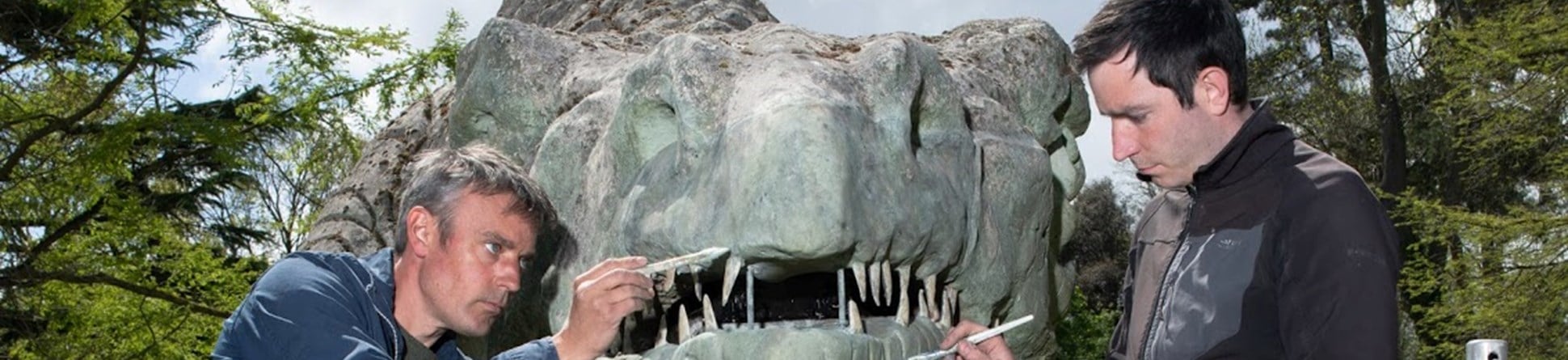 Photograph of the dinosaur sculpture's face as two skilled craftsmen intricately paint it's replacement jaw green.