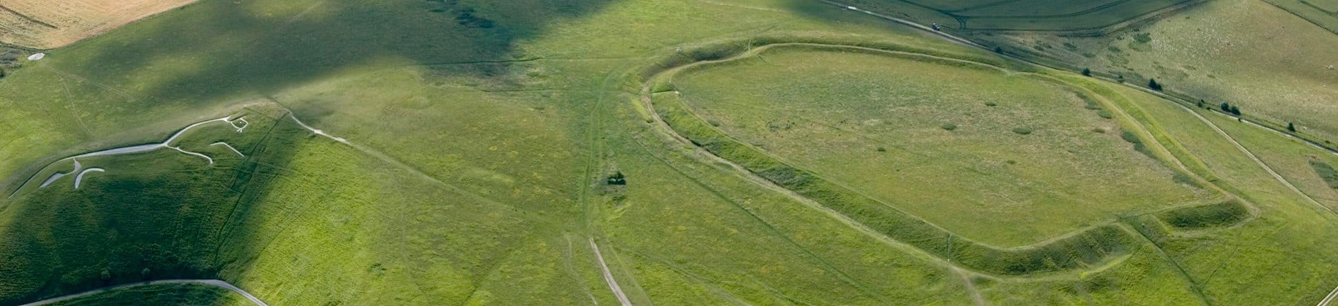 Colour aerial photograph showing a large banked earth enclosure to the right and a white chalk stylised figure of a horse left.