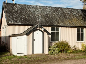 A small church made out of white corrugated walls and a black corrugated roof. 