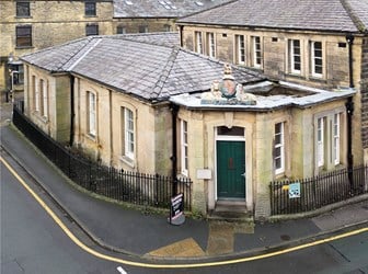 A low sandstone building with slate roofs on the corner of an urban street. 