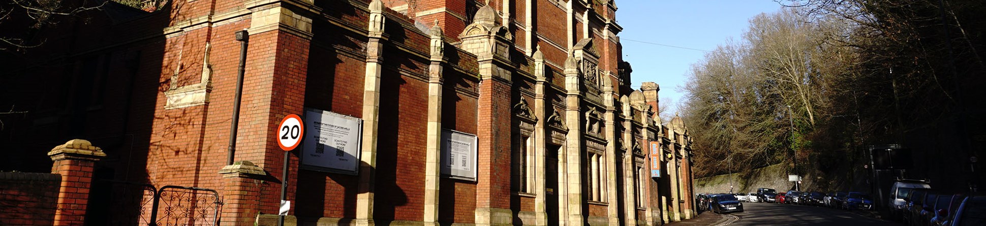 A photograph of the front of a large red brick building with ornate terracotta details facing onto an urban street. The roof has a temporary covering and the building is in poor repair.