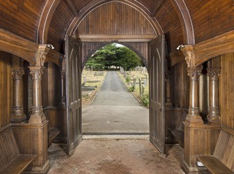 An ornate wood-pannelled room interior, with brick floor, opening onto a cemetery path.