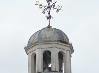 A photograph of a small octagonal bell tower on the rooftop of the Guildhall. It has round-headed openings and a domed lead roof, with an ornate weathervane on top.