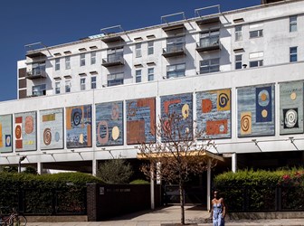 A multi-storey white residential building with panels on the facing side using primary colours and a selection of swirling and geometric patterns.