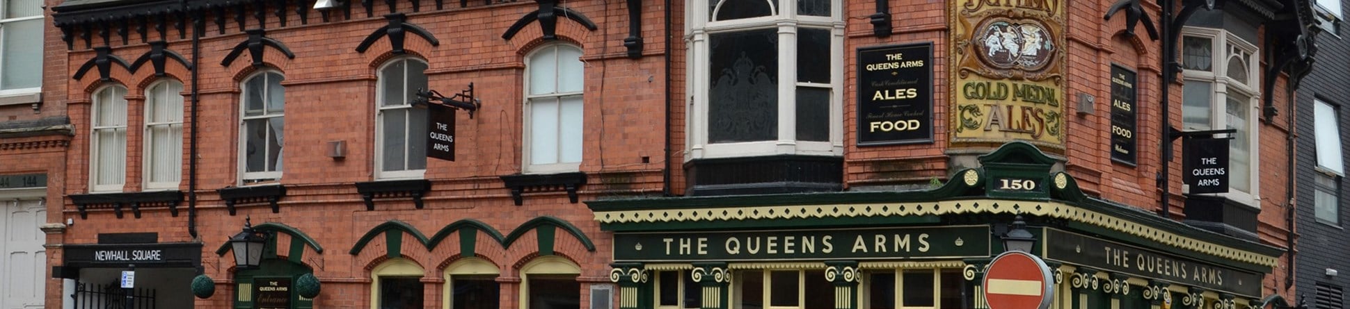A photo from street level of a pub in Birmingham with green frontage and bay windows on the ground floor