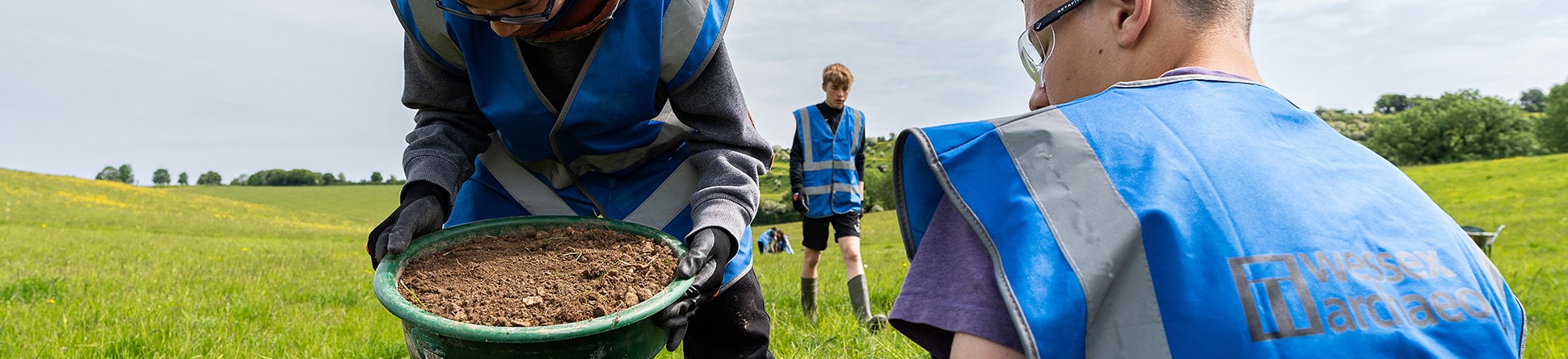 Young people sieving soil in a field as part of an archaeological dig.